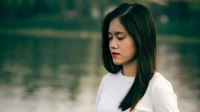 Woman standing with eyes closed and lake in background